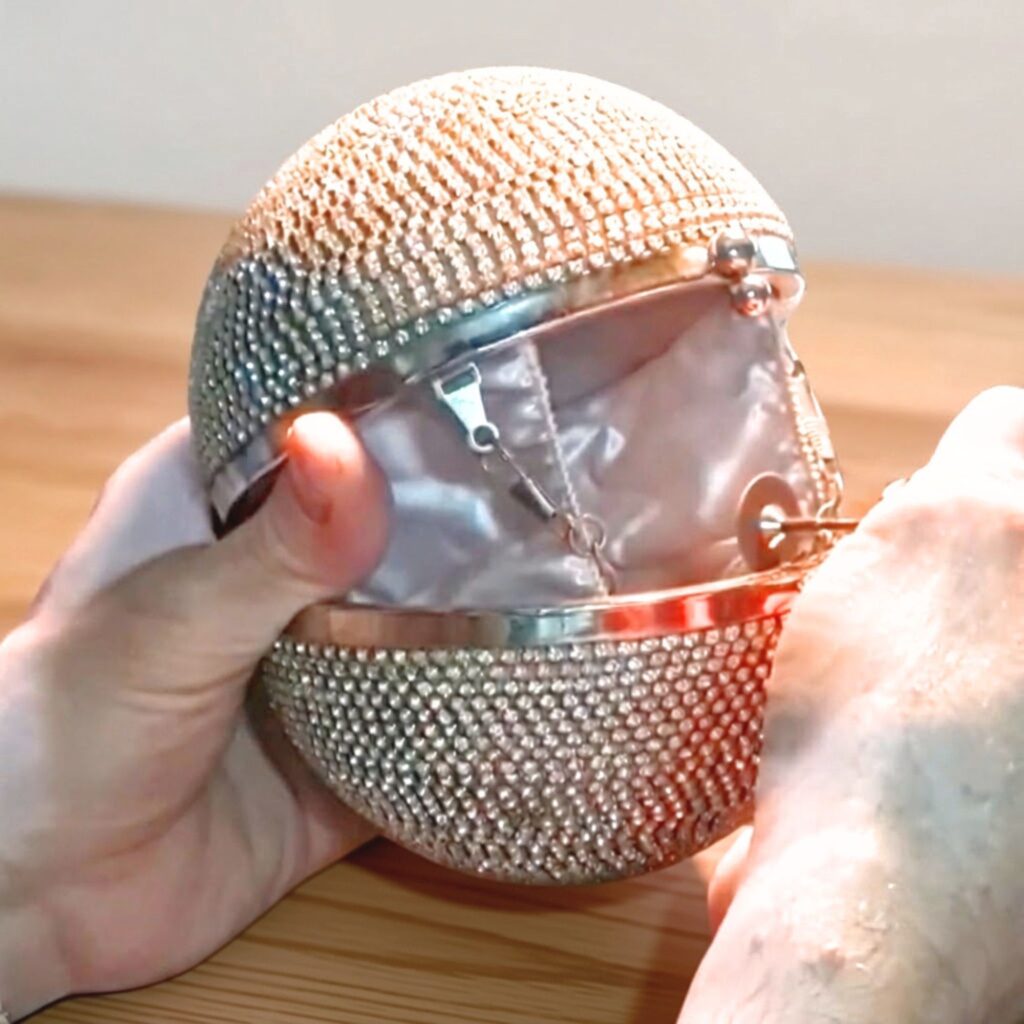 Se muestra un cartera de forma esférica toda de strass y que se reparó el cierre