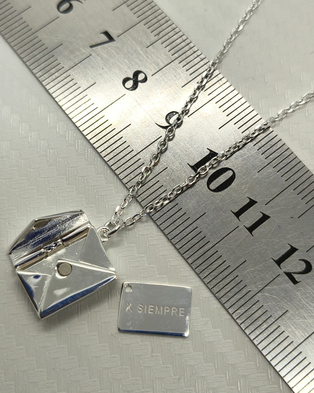 Collar de plata 925 con dije sobre con apertura y carta en su interior sobre regla para contexto de medida Collar de plata 925 con dije sobre con apertura y carta en su interior sobre regla para contexto de medida