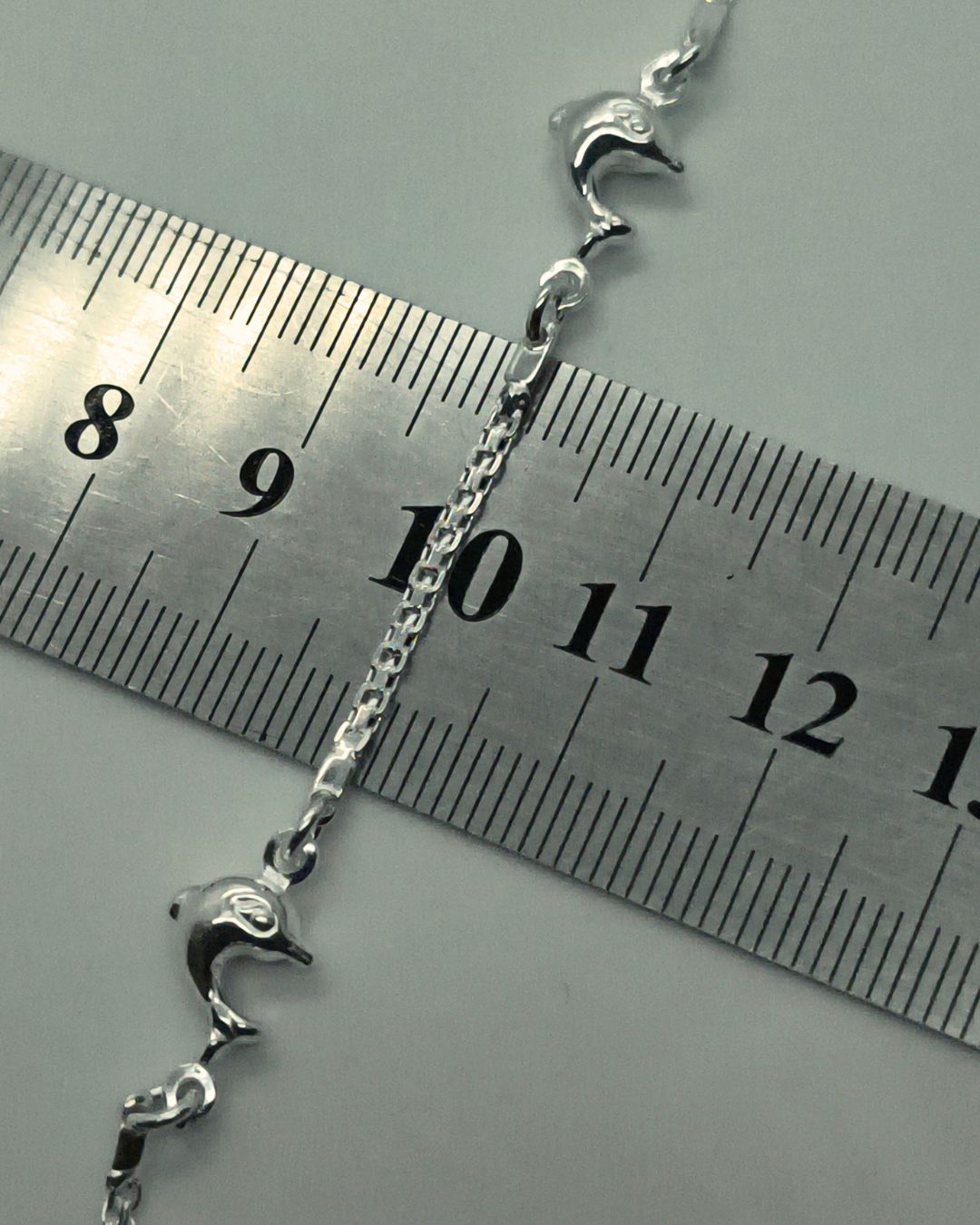 Pulsera de plata 925 con tres delfines alternados sobre regla para contexto de medida Pulsera de plata 925 con tres delfines alternados sobre regla para contexto de medida