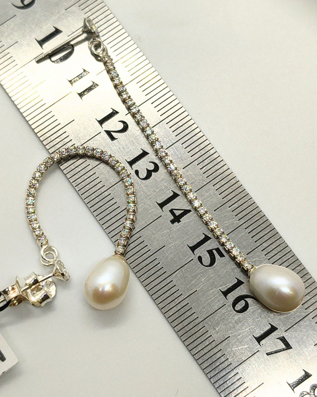 Aros de plata 925 laargos de tira de chatones con circonias y perla de rio en forma de gota sobre regla para contexto de medida Aros de plata 925 laargos de tira de chatones con circonias y perla de rio en forma de gota sobre regla para contexto de medida